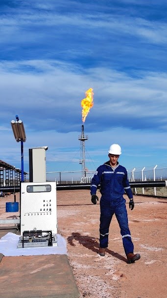 Manuel Rodriguez en una locación de Oil & Gas, con casco y ropa de trabajo, junto a un tablero y una antorcha de gas